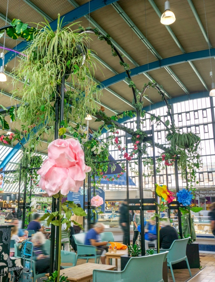 Eating area covered in foliage and flowers, and stalls in a large indoor market.