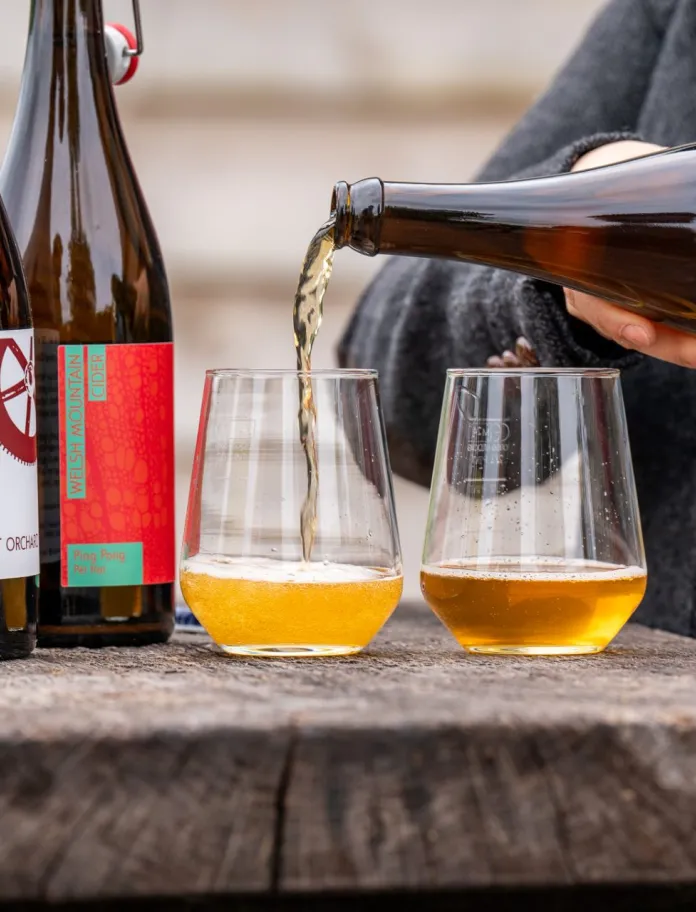Range of cider bottles with one being poured into a couple of glasses.