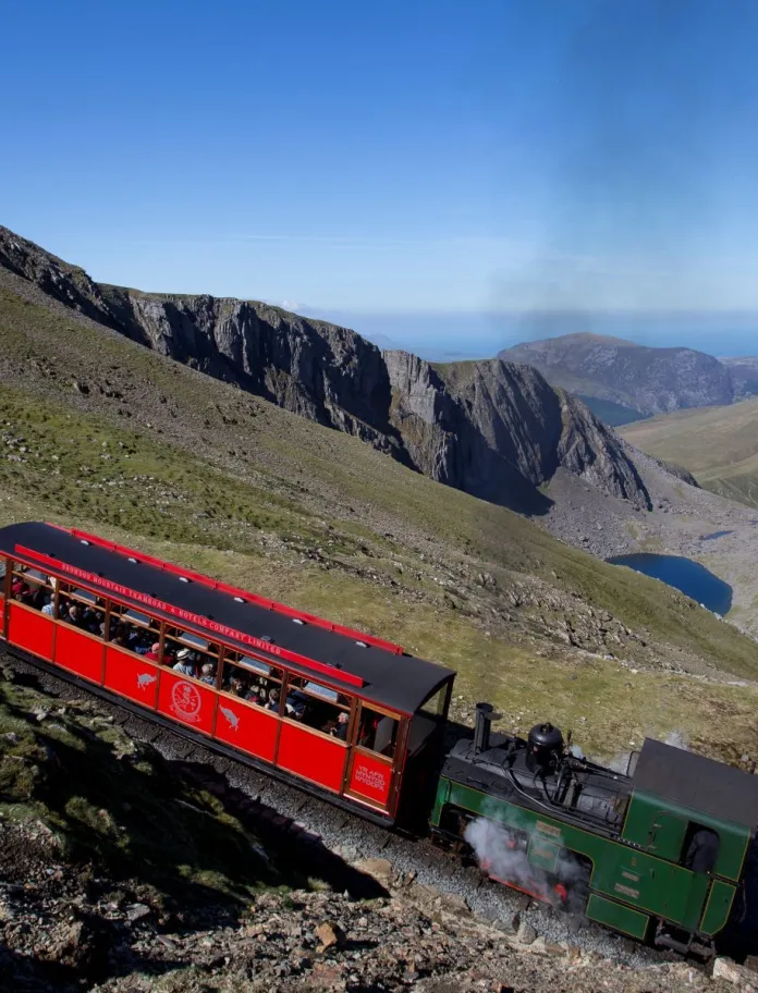 A diesel train taking passengers in a carriage up a mountain.