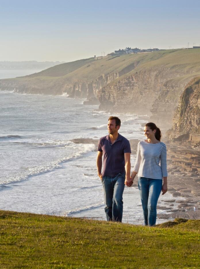 A couple walking on a coastal path with jurassic cliffs beyond.