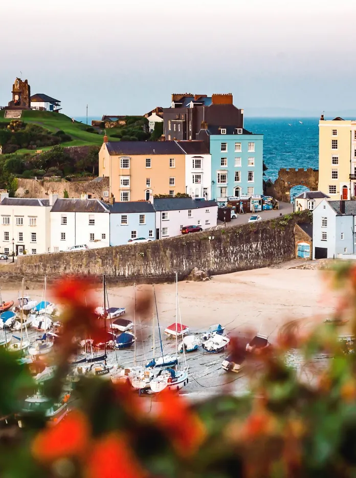 Looking down toward a harbour with boats on the sand and colourful houses and the sea in the background.