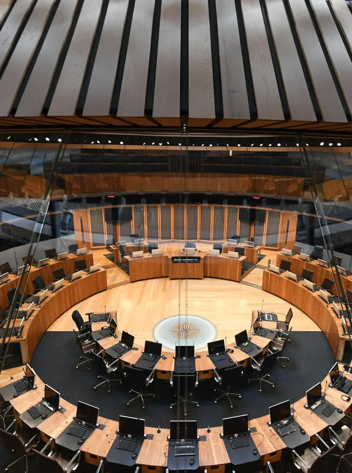 Chairs and tables set in a circle inf the debating chamber of a parliament building.