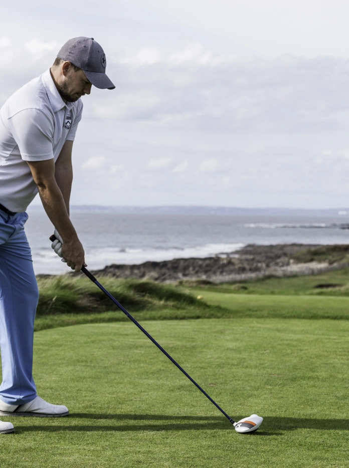 Golfer about to take a swing at the ball on the course alongside the coastline.