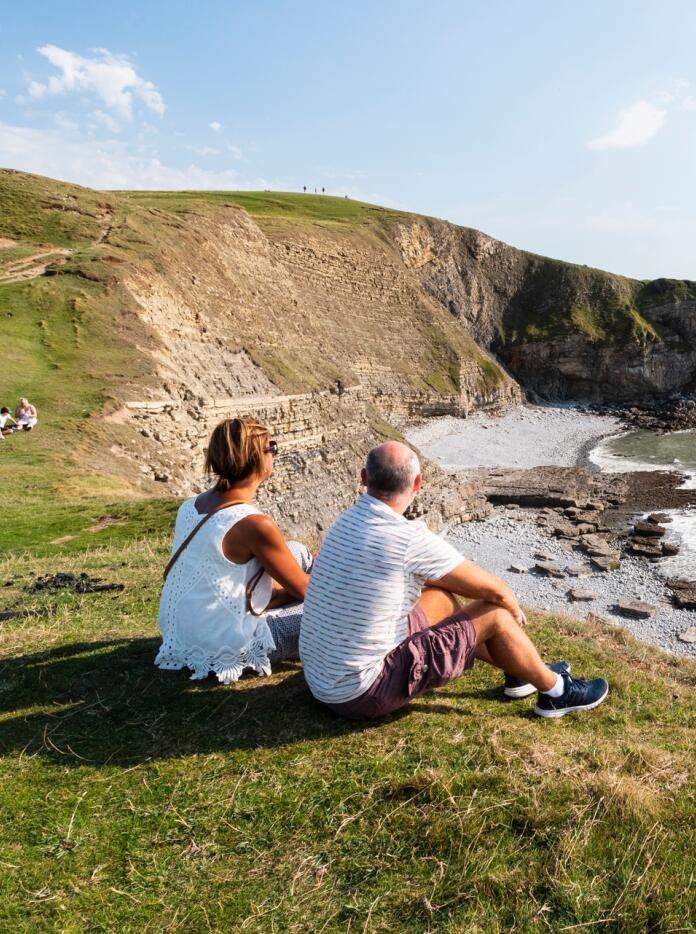 A couple sitting on the headland looking at the coast.