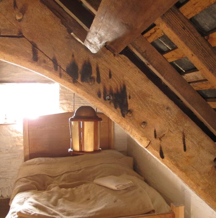 An old attic bedroom with a small window, beams and a lantern hanging over the bed.