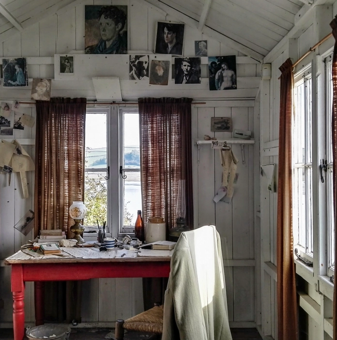 An inside scene of a shed with a writing desk and photographs on the wall.