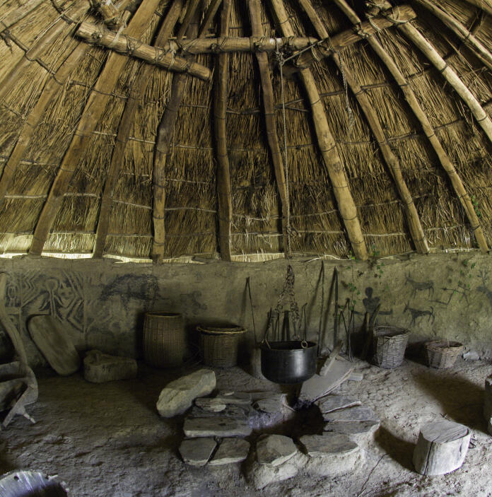Interior of iron age hut reconstruction with pots, stones and hieroglyphic drawings.