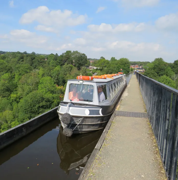 A narrowboat travelling along an aqueduct on a sunny day.