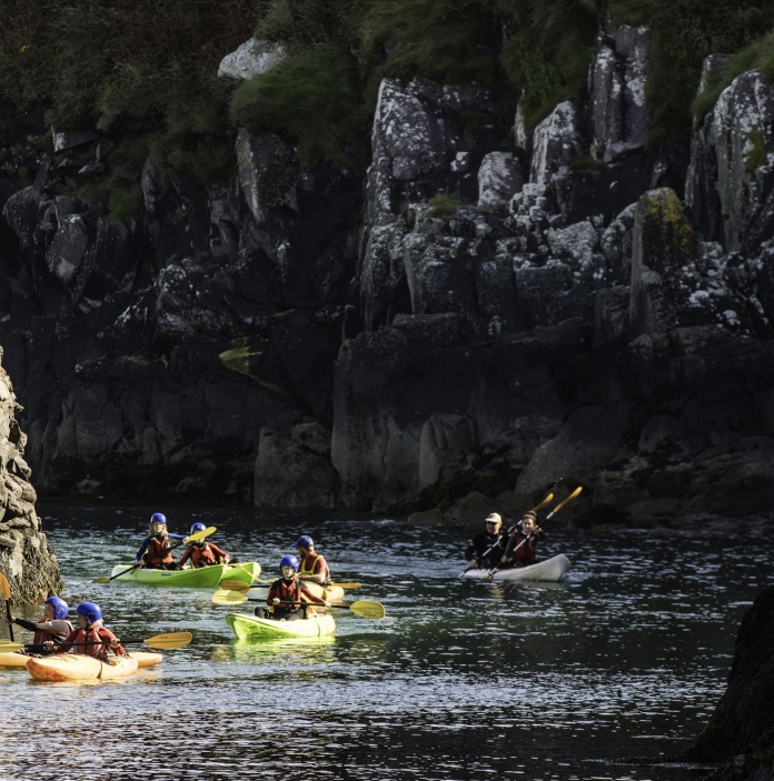 several people kayaking, with cliff face in background.