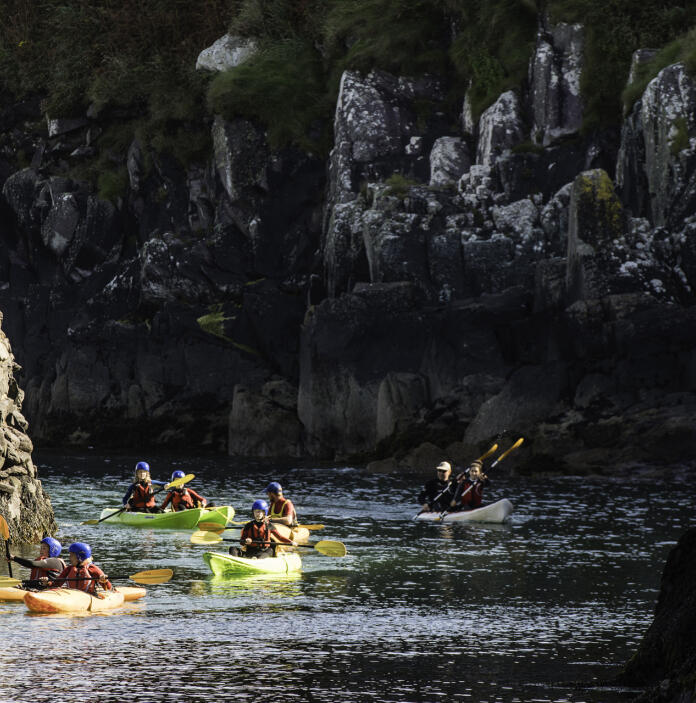 several people kayaking, with cliff face in background.