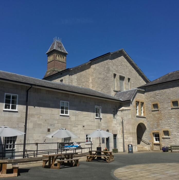 External view of a gaol and courtyard featuring picnic benches and parasols.