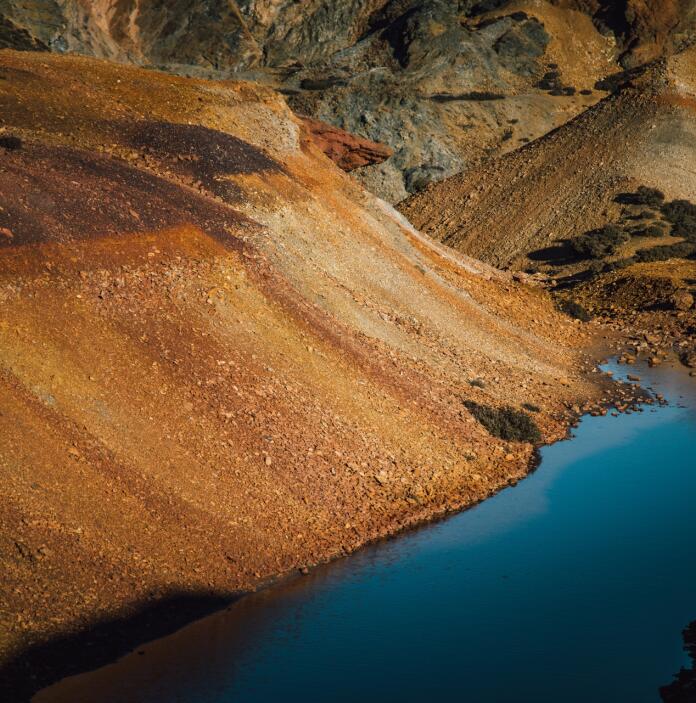 A mountain of colourful slate shingle next to a blue reservoir.
