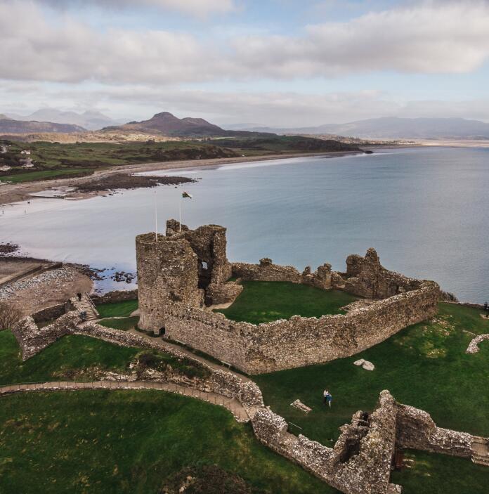 Aerial shot of a castle, the coast and mountains beyond.