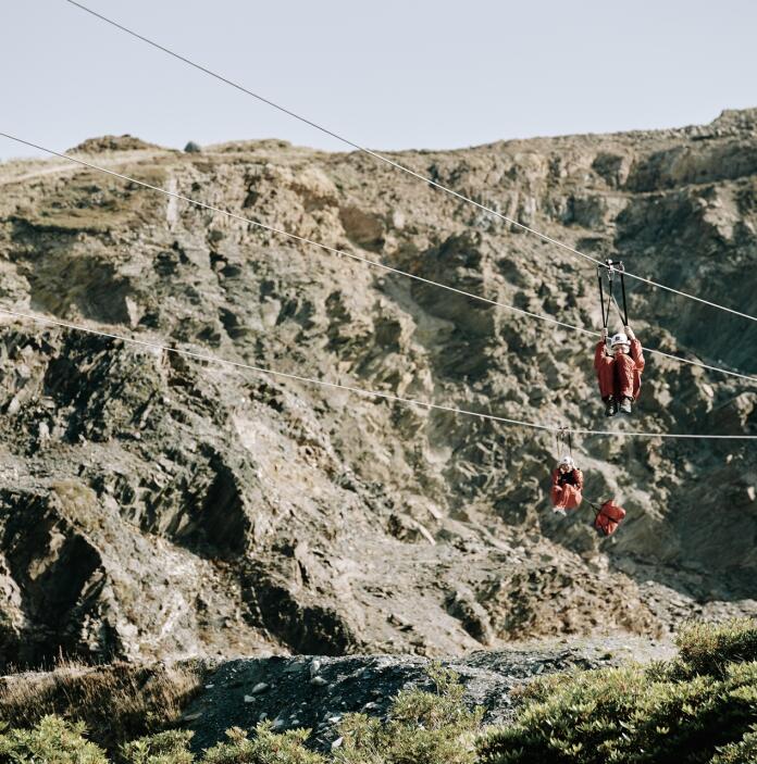 Four adventurers travelling down zip liners by a quarry.