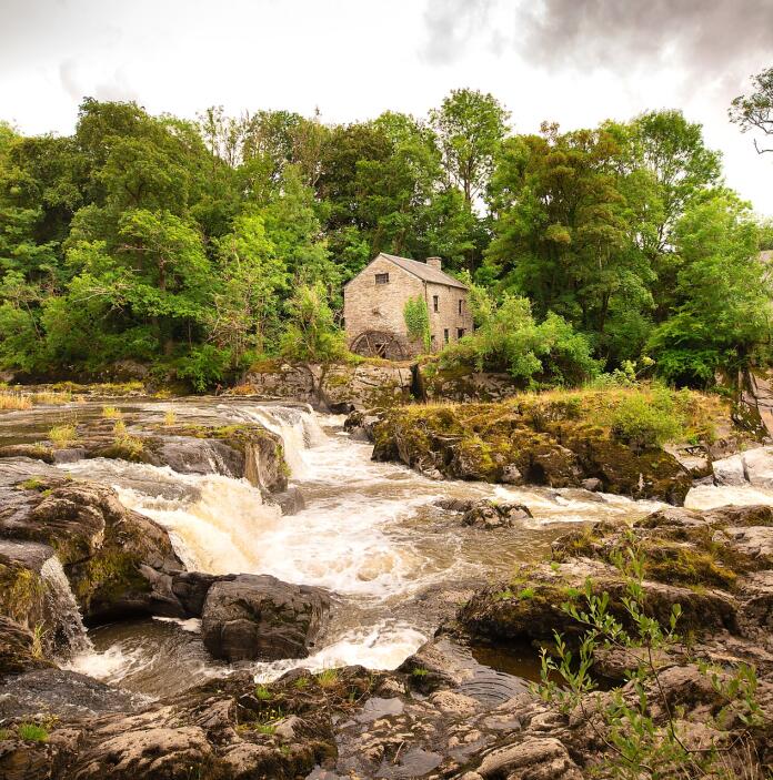 A watermill above the flowing river and rocks.