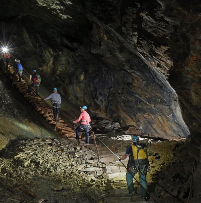 Visitors in safety gear climbing steps in an underground mine.