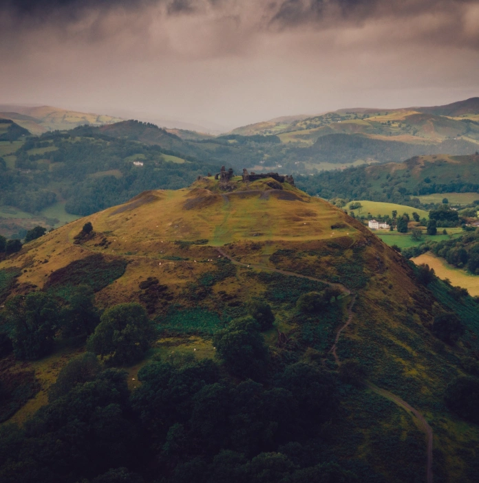 Ruins of a castle on a hill with mountains and countryside beyond.