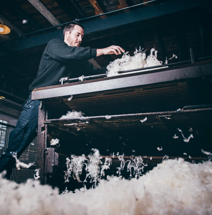 A worker shredding wool on a machine in a museum.
