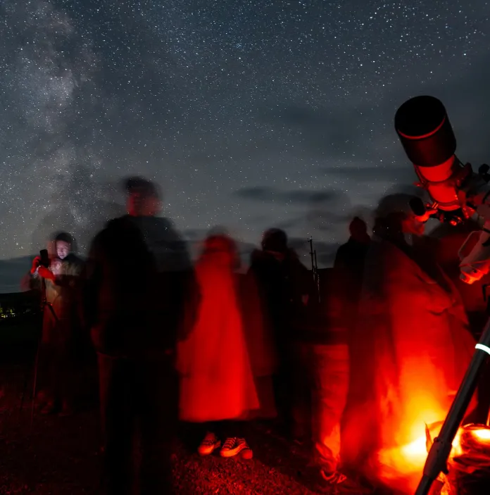 People standing by a telescope looking up to a starry sky at night.