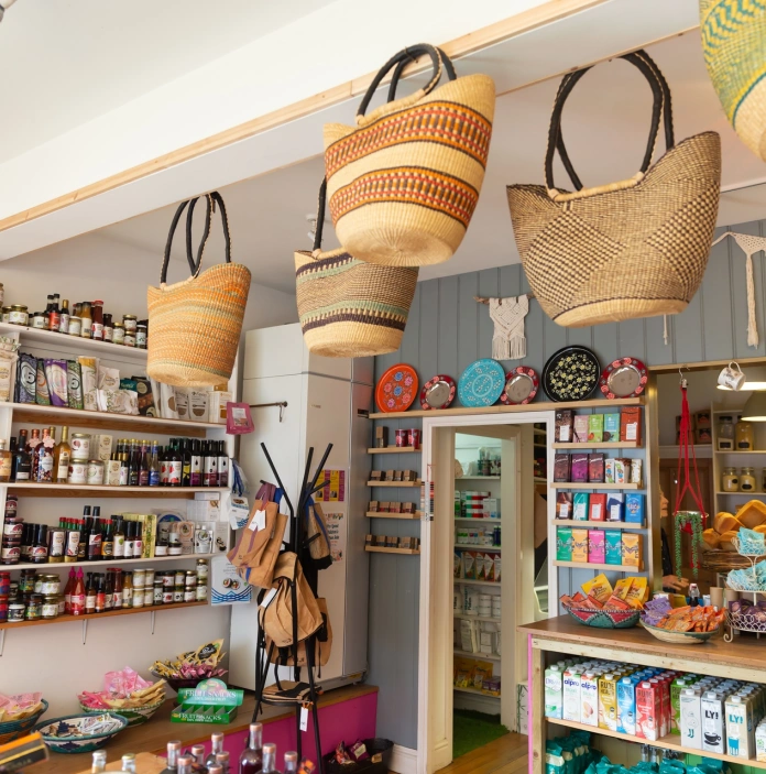 A shop with food and drink displayed on shelves, and hessian baskets hanging above.,