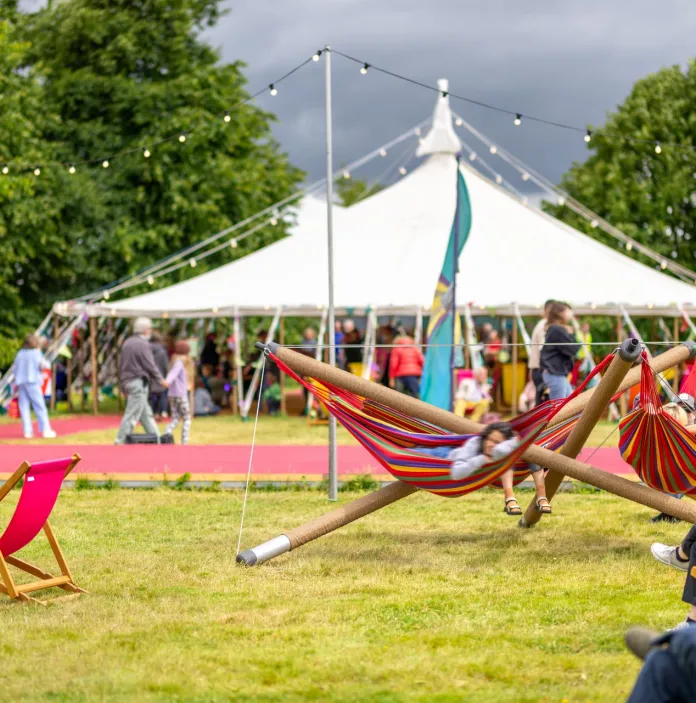 Deckchairs on a lawn next to a marquee, with people walking and sitting.