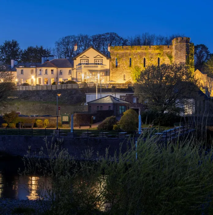 External shot of a castle hotel lit up at night, with a river running beside it.