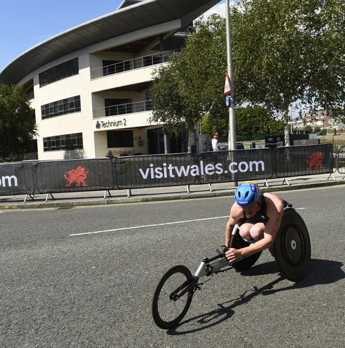Rider with an accessible bicycle cycling past buildings on a road in a race.