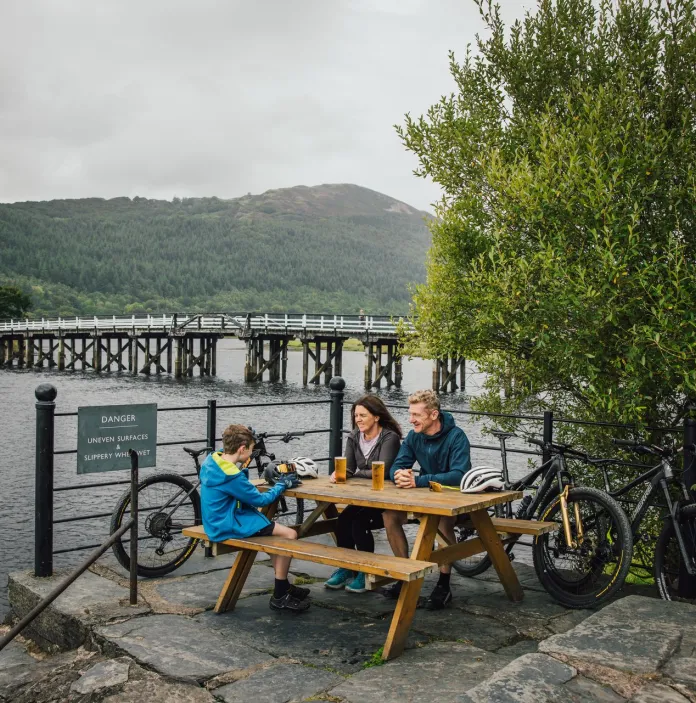 A family sitting on a picnic bench with their bikes, with views of an estuary beyond.