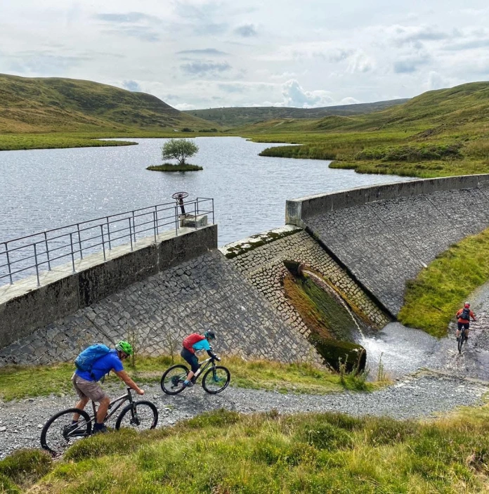 Cyclists heading down a gravel path next to a dam.