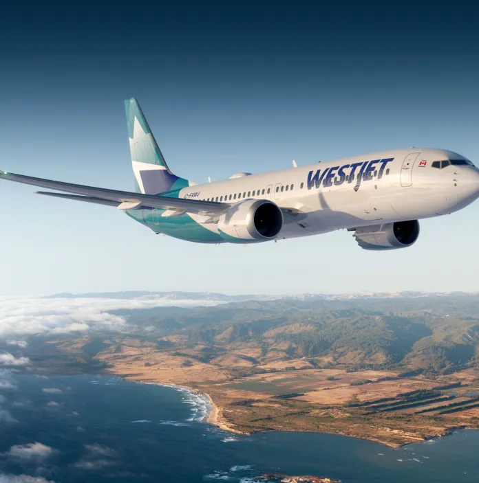 An aircraft in the sky above the sea and coastline.