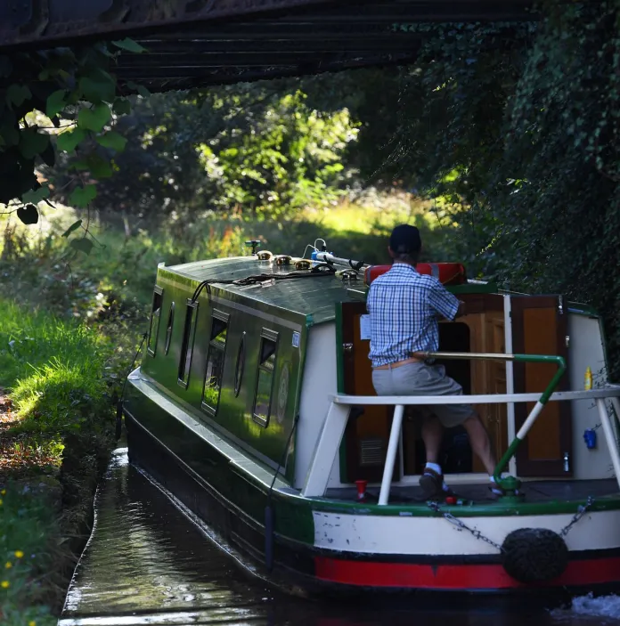 A cyclist on a path by a canal with a barge sailing past.