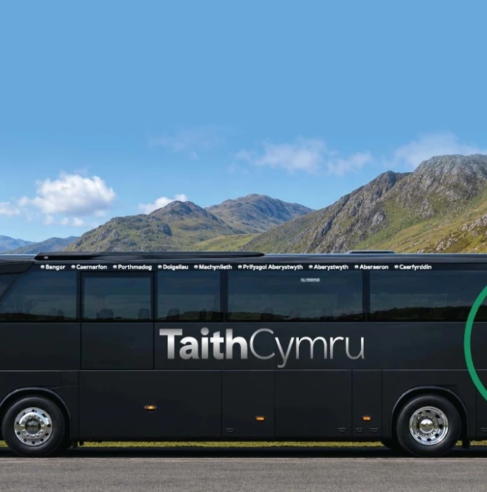 A coach parked up with views of mountains and a lake beyond.