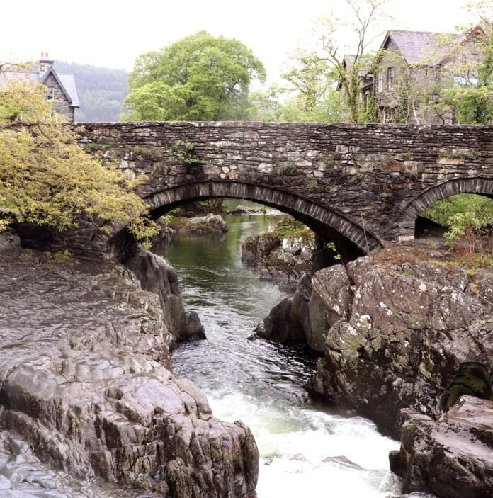 A river running through a stone bridge between rock formations in a pretty village.