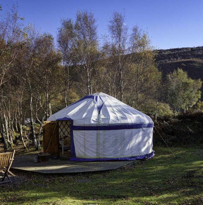 A white yurt with seating outside surrounded by trees at Graig Wen.