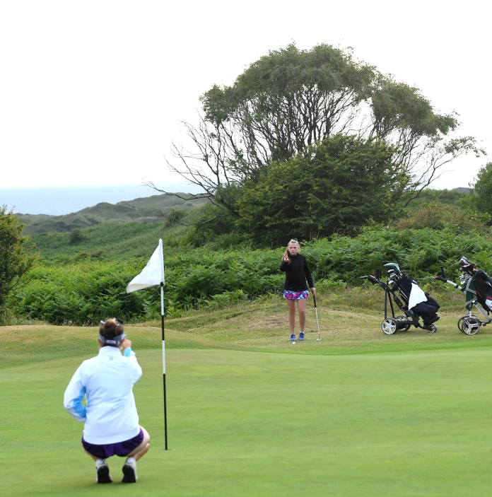 Golfers on the green lining up the shot to put the ball in the hole.