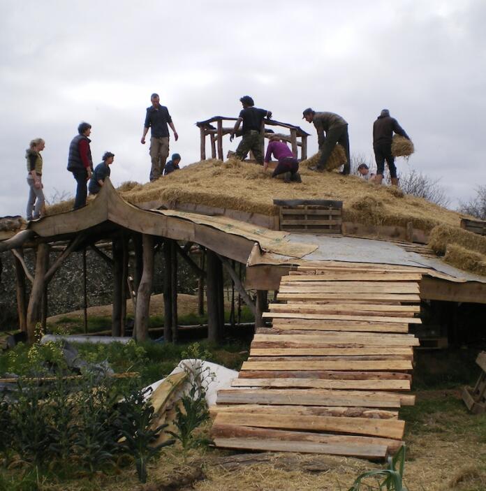 people laying a strawbale roof on a building.