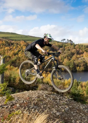 A mountain biker doing a jump amongst forestry.