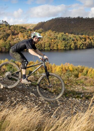A mountain biker riding downhill with a reservoir and mountains beyond.