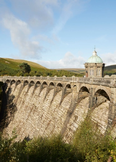 A dam holding back the water of the reservoir amongst hills beyond.