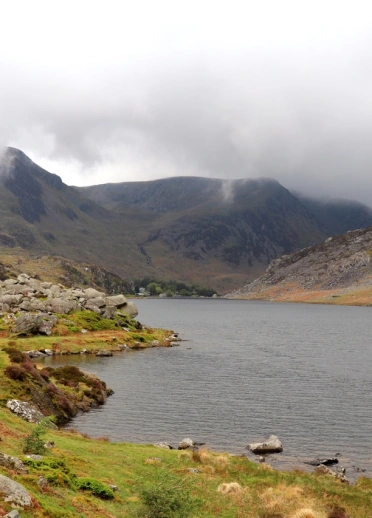 Views of a lake with mountains shrouded in low cloud beyond.