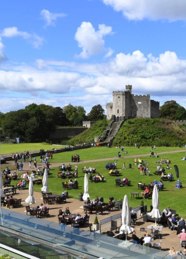 A castle and its keep behind lawns filled with people sitting on tables.