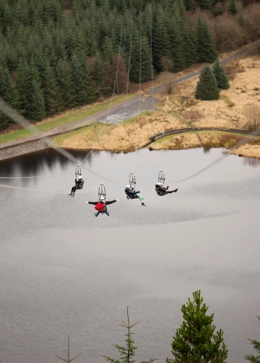 Four people travelling down a zip line above a lake.