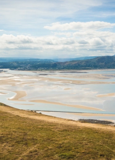 Two people looking at the ocean and mountains beyond from a coastal path.