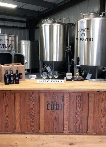 A bar in a taproom with beer brewing vats behind.