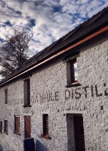 A white stone cottage with several small windows and a Mhile Distillery marked on the wall.