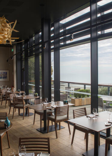 A dining room in a restaurant by the coast with views of the sea.