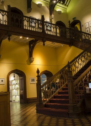 Grand staircase and landing in in Plas Glyn-y-Weddw art gallery with art on the walls.