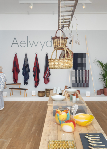 Display of crafts on table and wall with two women looking at wall artwork at Ruthin Craft Centre.