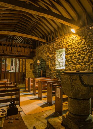 Interior of a church with wooden beams and pews and natural stone walls and fountain.