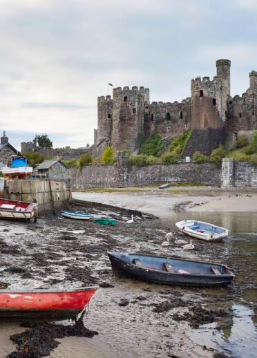 Views of a castle beyond an estuary with moored boats on its bank.